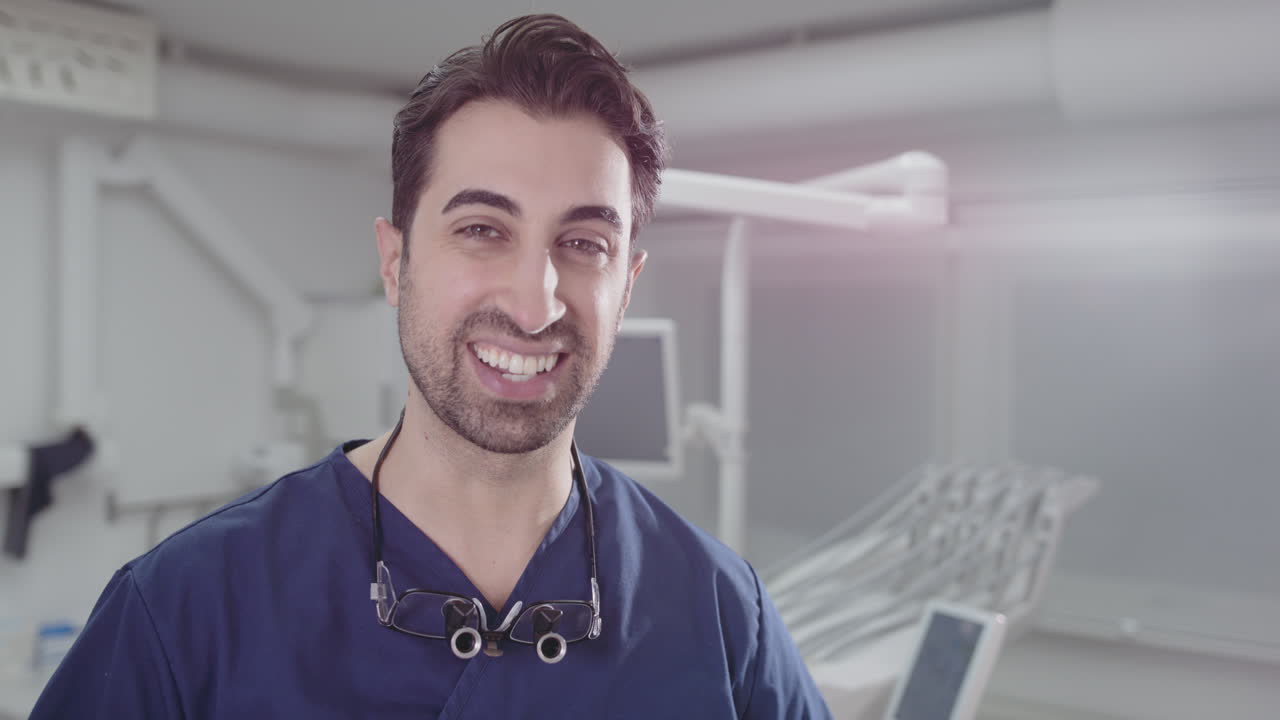 Patient POV friendly smiling dentist with loupes around neck inside clinic