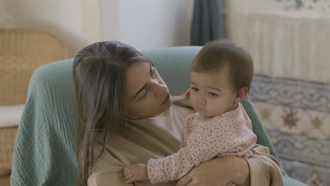 mamá amorosa sentada en un sillón, sosteniendo a su hija y hablando con ella