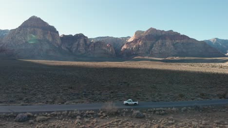 Aerial-drone-shot-of-Red-Rock-Scenic-Highway-with-mountains-in-the-background