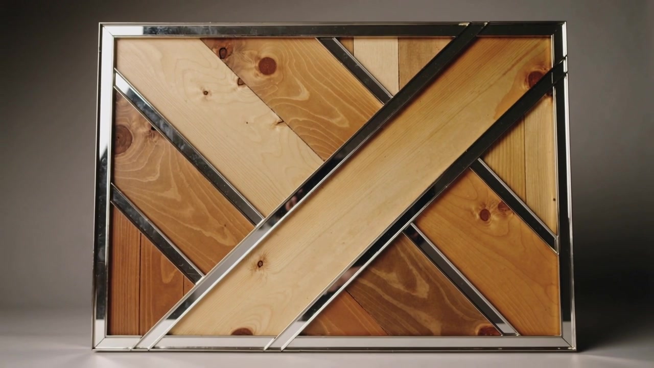 La telecamera si allontana rivelando un pannello di legno incorniciato su una scrivania da studio per mostrare il design completo, con finiture cromate.