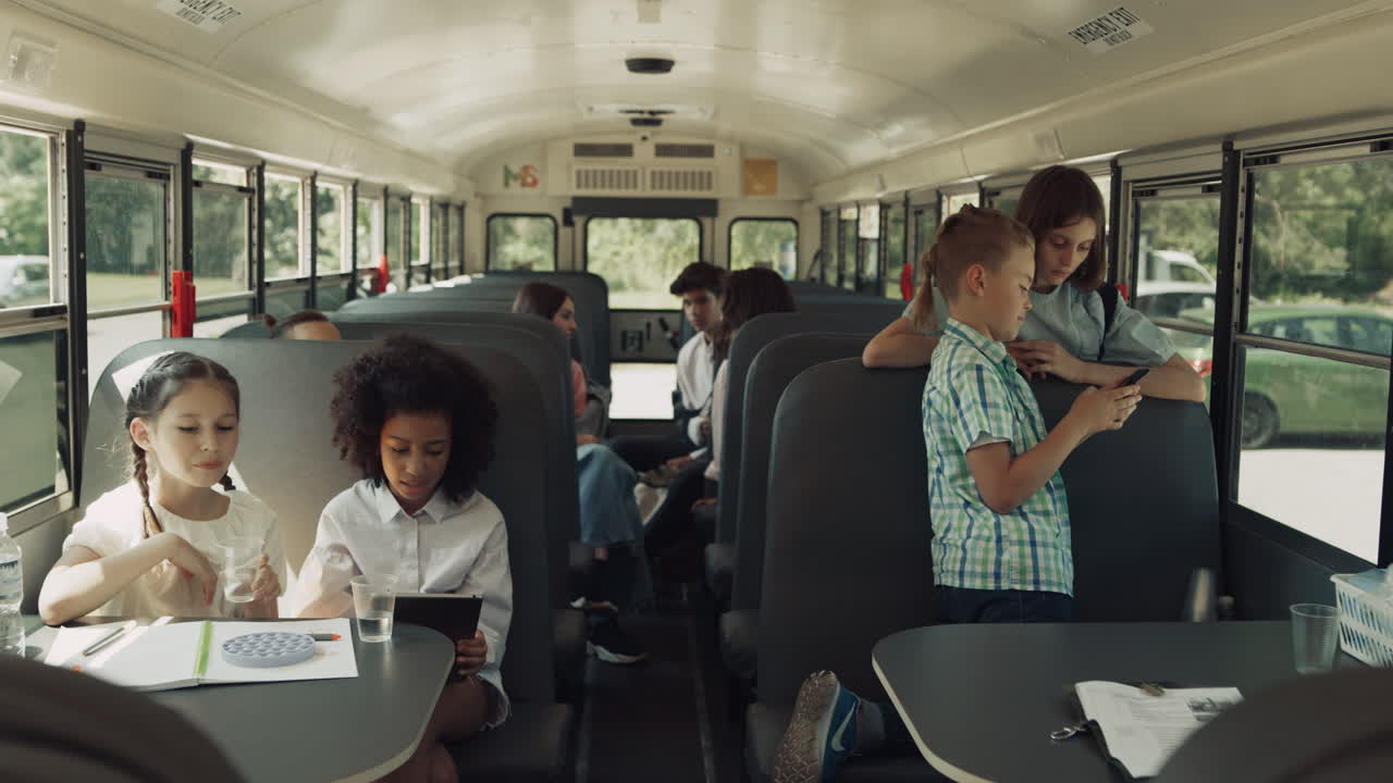 Tienerklasgenoten zitten in de schoolbus te praten. Multiculturele klas kletst en speelt.
