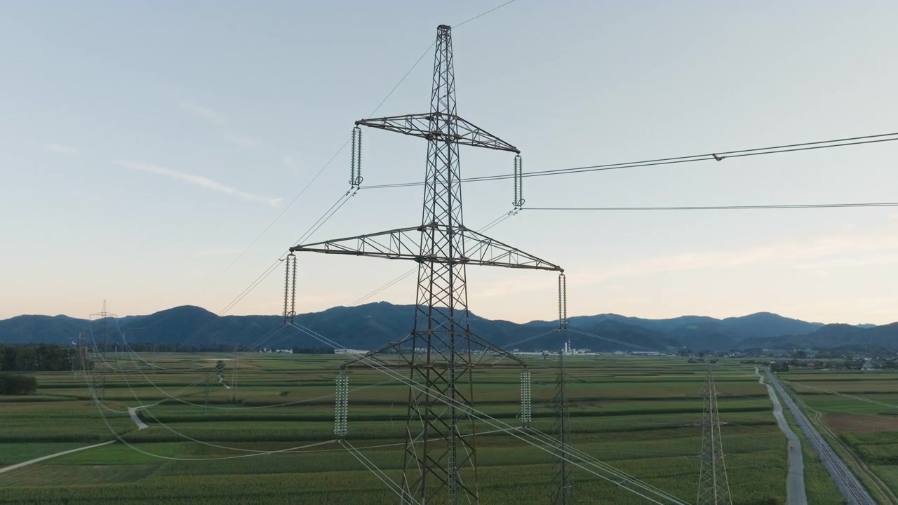 Power lines and towers are visible in a rural area as the sun sets in the background highlighting