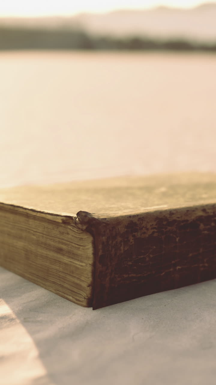 Un libro impolverato e antico appoggiato su sabbia calda e illuminata dal sole in un tranquillo ambiente costiero