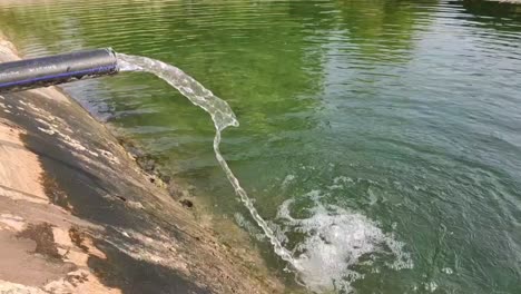 Wasser,-Das-Von-Einer-Motorpumpe-Aus-Dem-Schlauchrohr-In-Das-Rohr-Gelangt,-Grundwasservorrat-Im-Teich-Zur-Bewässerung-Der-Pflanzen,-4k