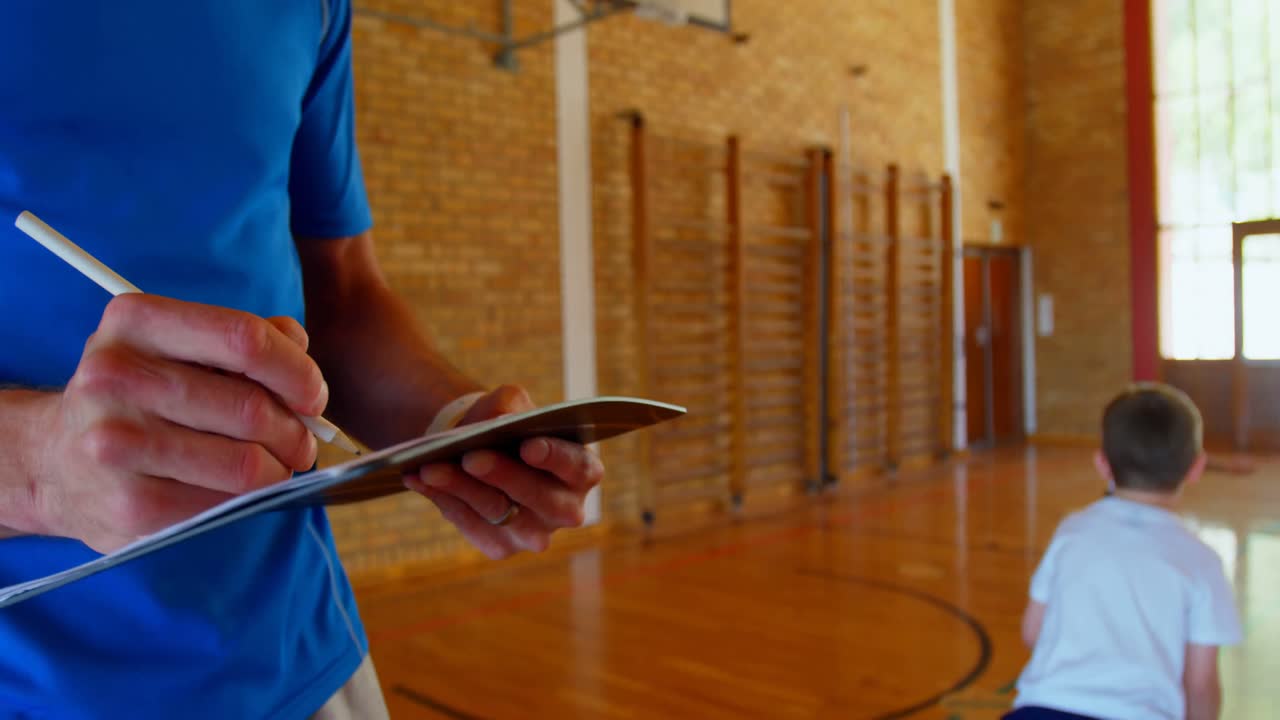 Basketball coach writing on a notepad in basketball court at school 4k