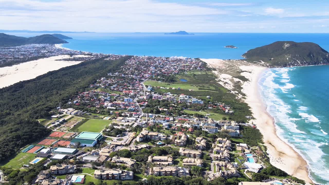 Cảnh quay điện ảnh từ trên cao thu lại toàn cảnh bãi biển Santinho ở Florianopolis, Brazil, hé lộ các khu dân cư ven biển, cồn cát, Morro dos Ingleses và Đại Tây Dương