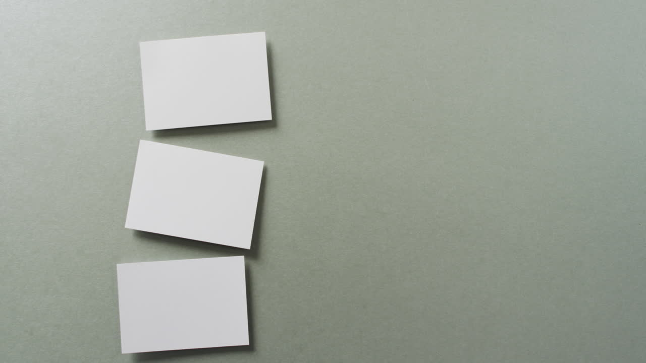 vista aérea de tres tarjetas de visita blancas dispuestas en fondo gris, espacio de copia, cámara lenta