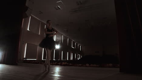 una joven bailarina profesional haciendo movimientos circulares en el escenario. una hermosa chica bailando bajo los reflectores por la noche durante el ensayo de vestuario.