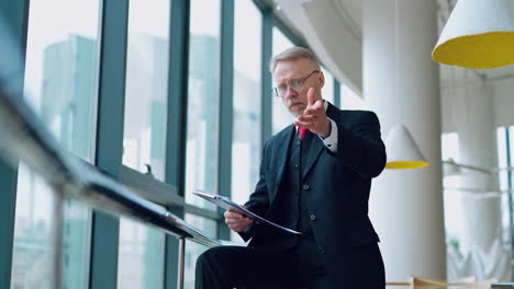 portrait of mature businessman near the window. elderly director in costume reading documents nervously and scattering them in the office.
