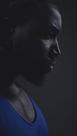 vertical video close up profile shot of determined male boxer or athlete training in gym preparing for fight or sports event against black studio background 1