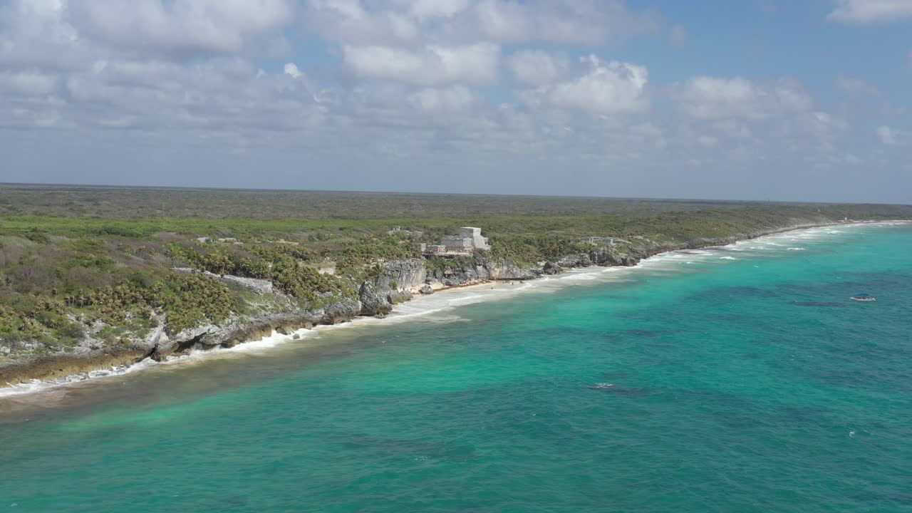 avance aéreo sobre aguas turquesas del mar caribe y ruinas mayas en el fondo, tulum