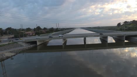 A-drone-glides-sideways-over-water-as-cars-drive-over-a-bridge