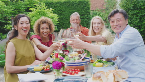 portrait of mature friends making a toast with wine at summer party in garden at home