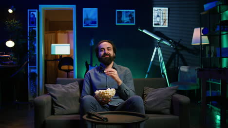 man laughing at funny shows on television, eating snack, sitting on couch