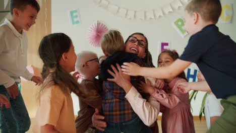 a group of children hug their teacher, a blonde woman with a bob hairstyle in glasses in a white shirt at their first lesson in a club for preparing children for school classes. the children love their woman teacher and hug her during a preschool lesson