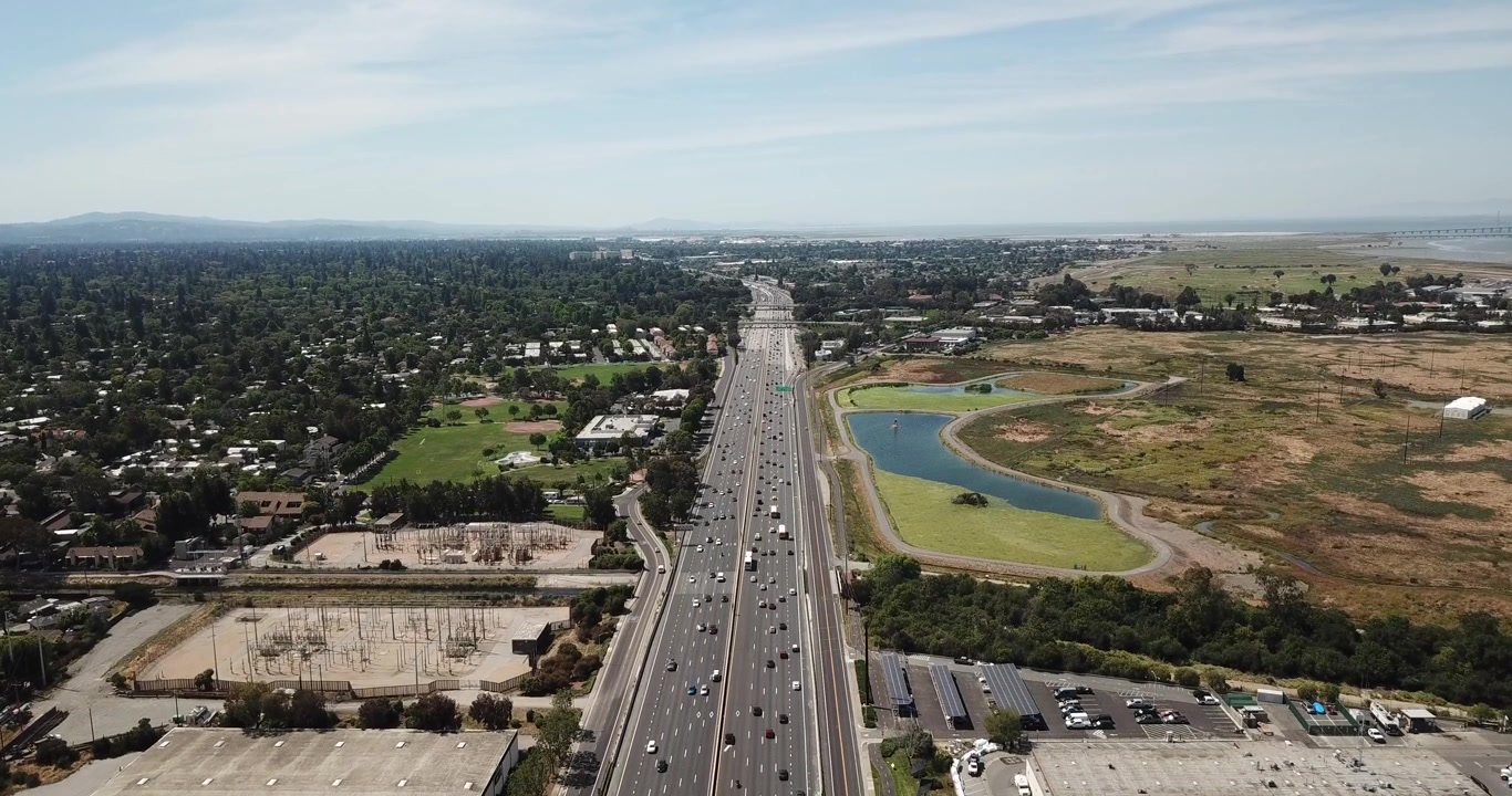 Aerial view of suburbs dense trees rooftop houses pine trees cars freeway 101 marsh electric transformers hold hover