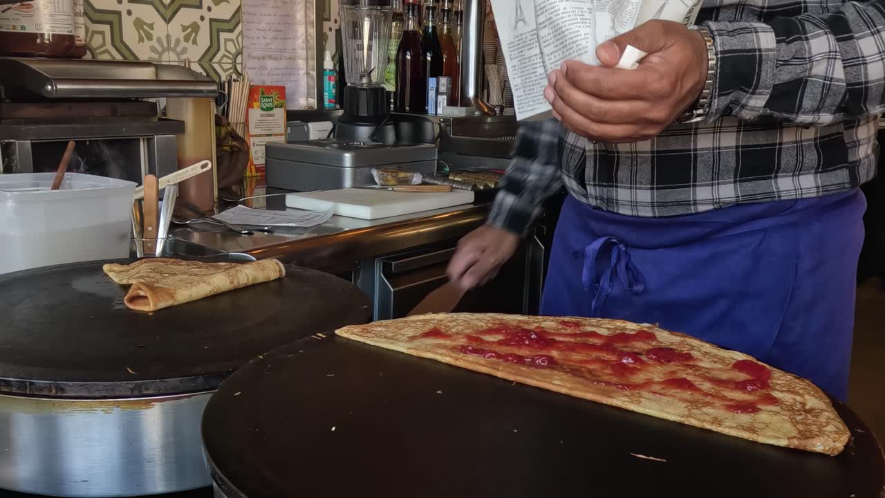 A vendor skillfully folds and serves crepes with a spatula at a bustling food stall.