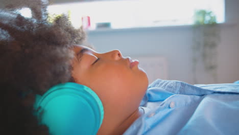 Niño-Acostado-En-La-Cama-Usando-Auriculares-Inalámbricos-Con-Los-Ojos-Cerrados-Escuchando-Música-O-Audiolibro