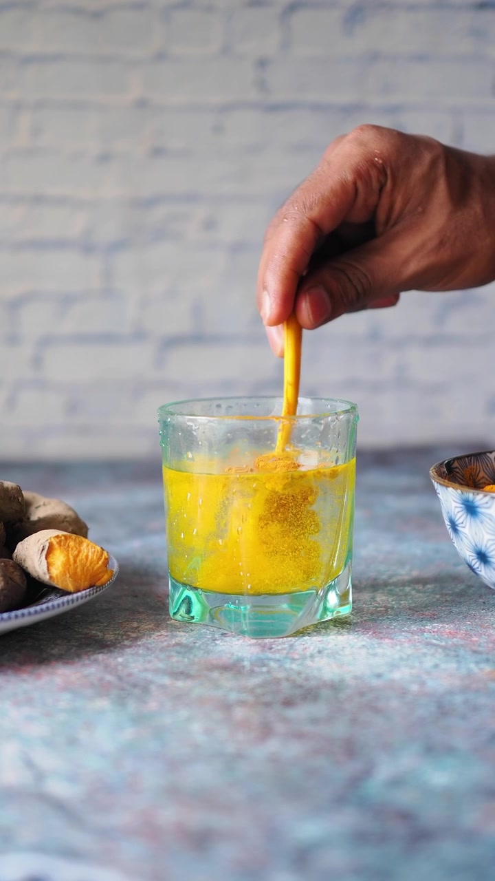 Removiendo a mano cúrcuma en polvo en un vaso de agua
