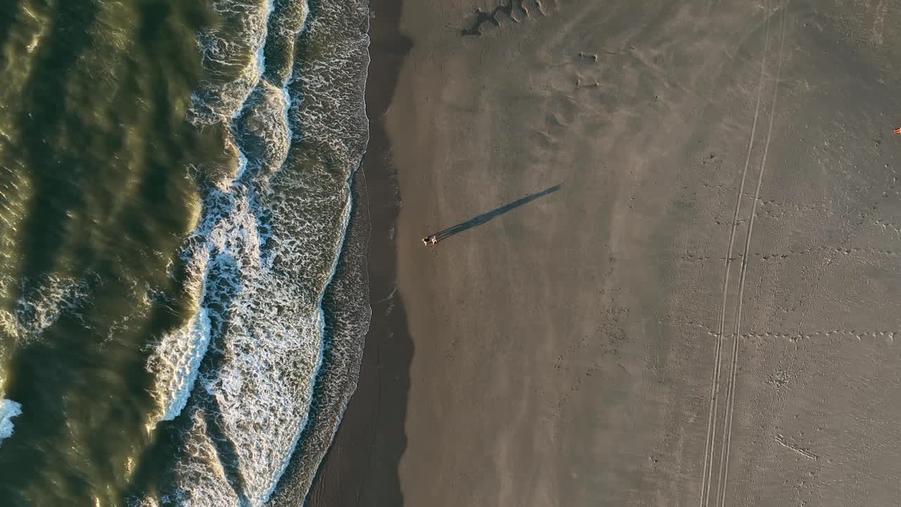 Tramonto che proietta lunghe ombre di una coppia che cammina sulla spiaggia, vista aerea dall'alto