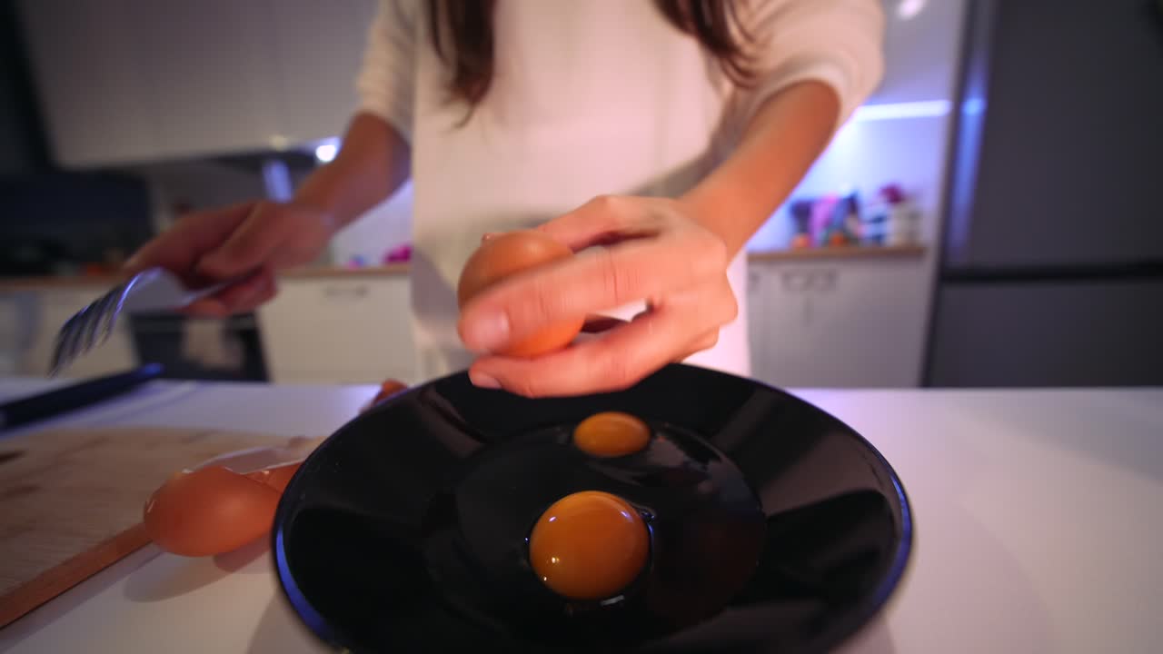 Close-Up of Hands Cracking Eggs into a Black Plate in a Modern Kitchen