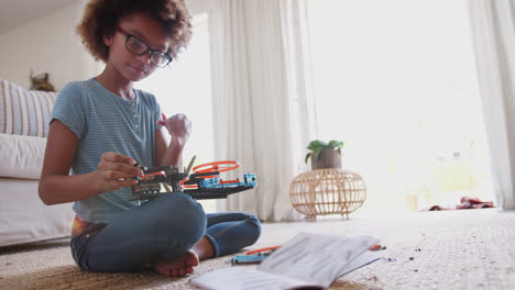 niña afroamericana pre-adolescente sentada en el suelo construyendo un juego de kit de construcción, de cerca, en toda su longitud