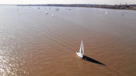 Sailboat-cruising-on-muddy-river-waters---aerial