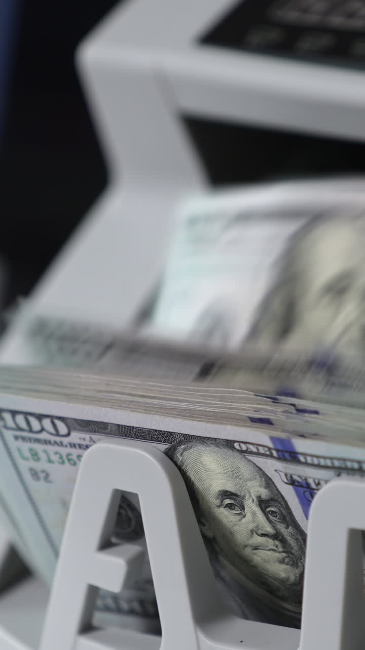 Switched on money counting machine. Hundred dollar bills turning in the counting mechanism. Close up. Vertical video