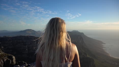 slowmotion pulling back from a young blonde woman sitting and looking the view on the table mountain during sunset