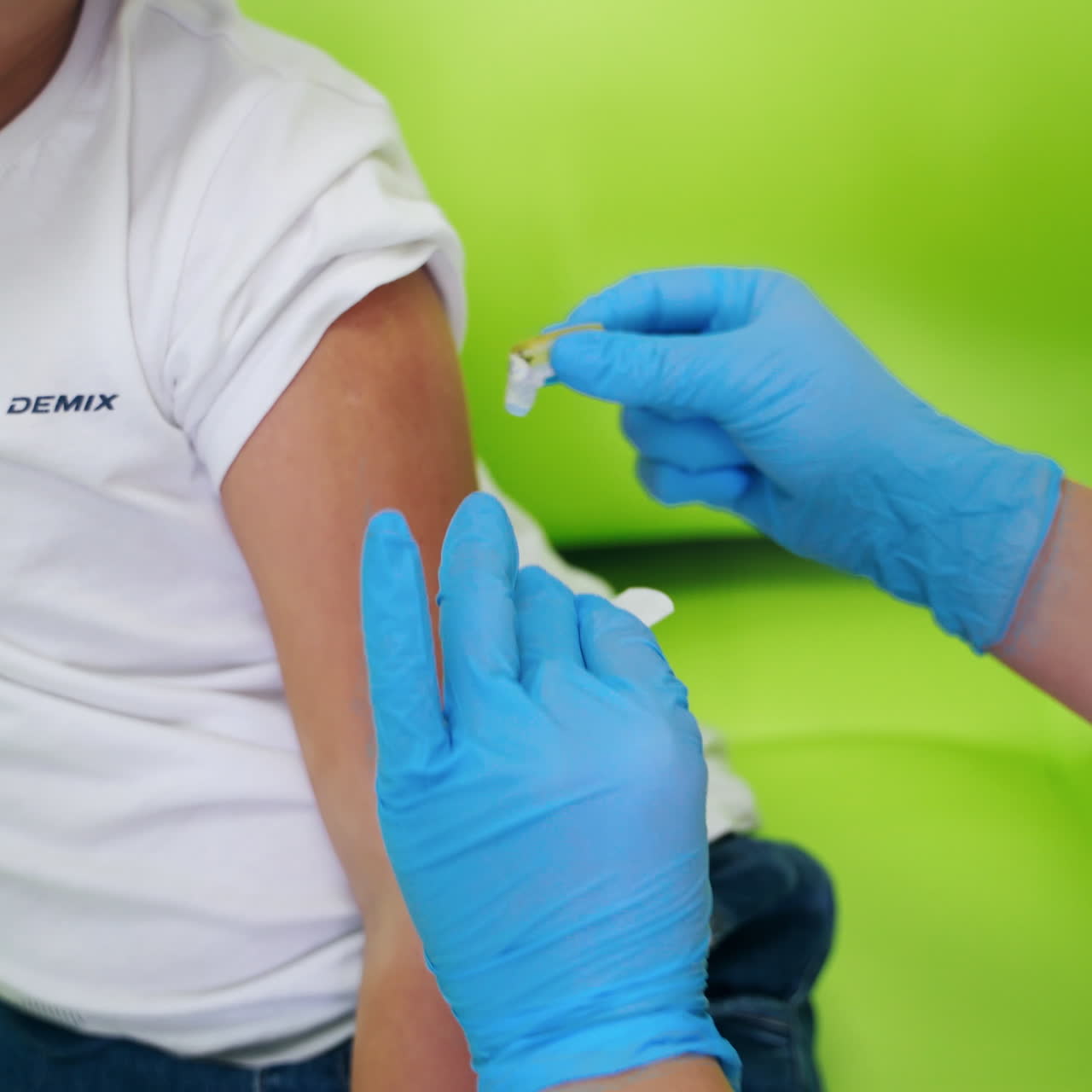 Female doctor doing an injection. Nurse worker in blue sterile gloves pricking needle into boy's arm. Medical procedure of injection. Close-up.