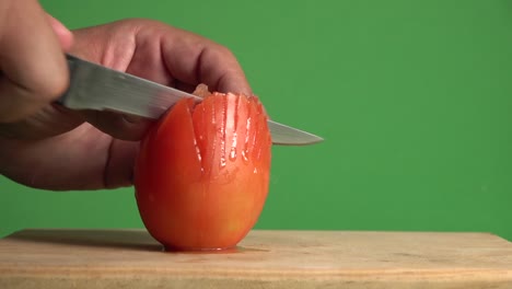 a hand vertically slicing through a tomato on a chroma background