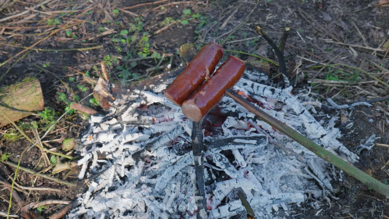 Grilling sausages on a stick over a campfire, outdoor cooking on a sunny day