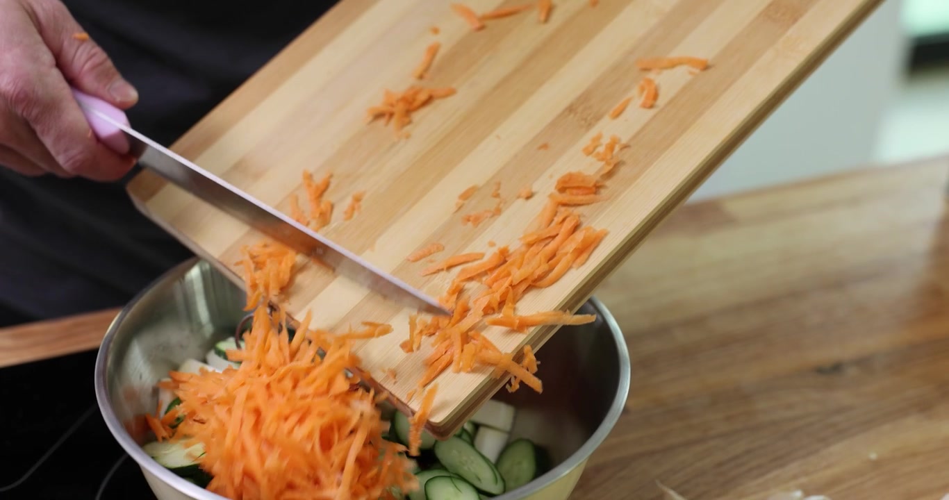 Chef transfers grated carrot from cutting board into bowl