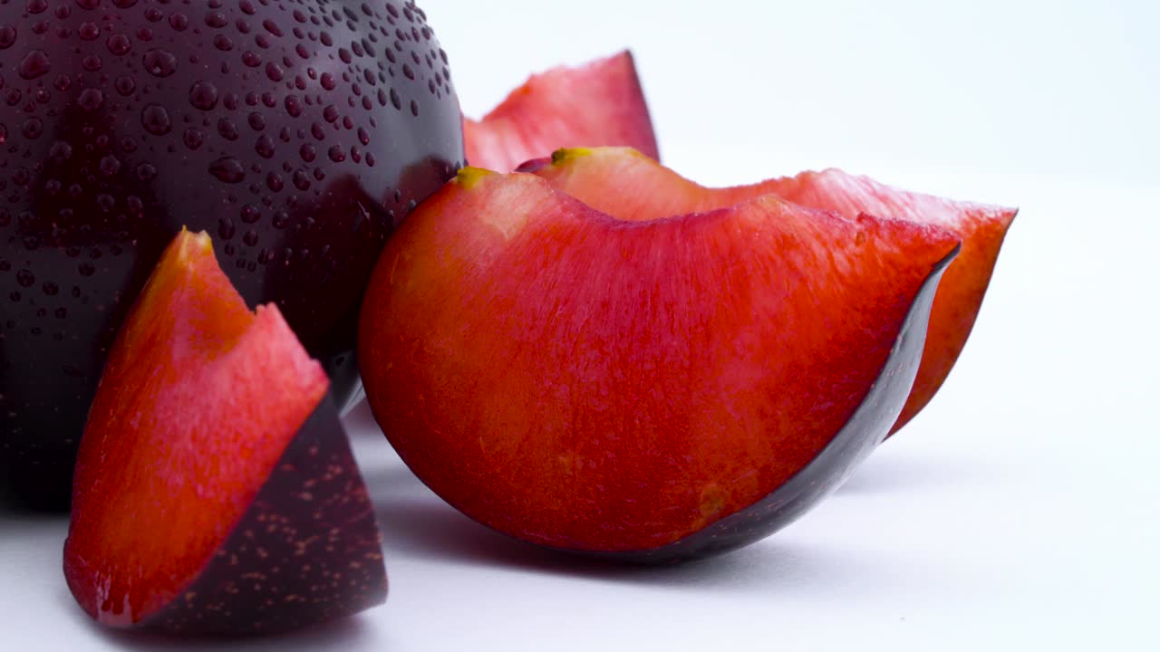 macro disparo de un todo y algunas pequeñas partes de gran ciruela púrpura maynard con gotas de agua. girando lentamente en la mesa giratoria aislada en el fondo blanco. primer plano.