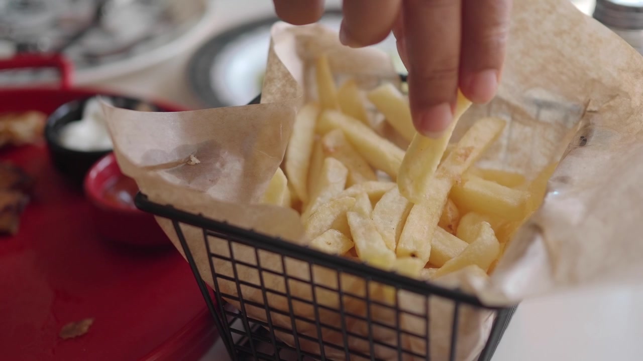 Hand Picking a French Fry from a Metal Serving Basket