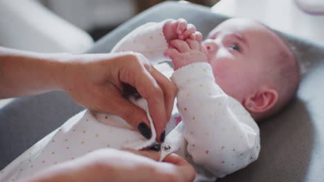 close up of mother’s hands doing up her baby’s onesie after changing him, baby smiling