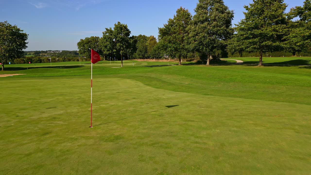 Green da golf con asta portabandiera ed erba curata sotto un cielo terso su un campo tranquillo, ripresa aerea, vuoto, senza nessuno