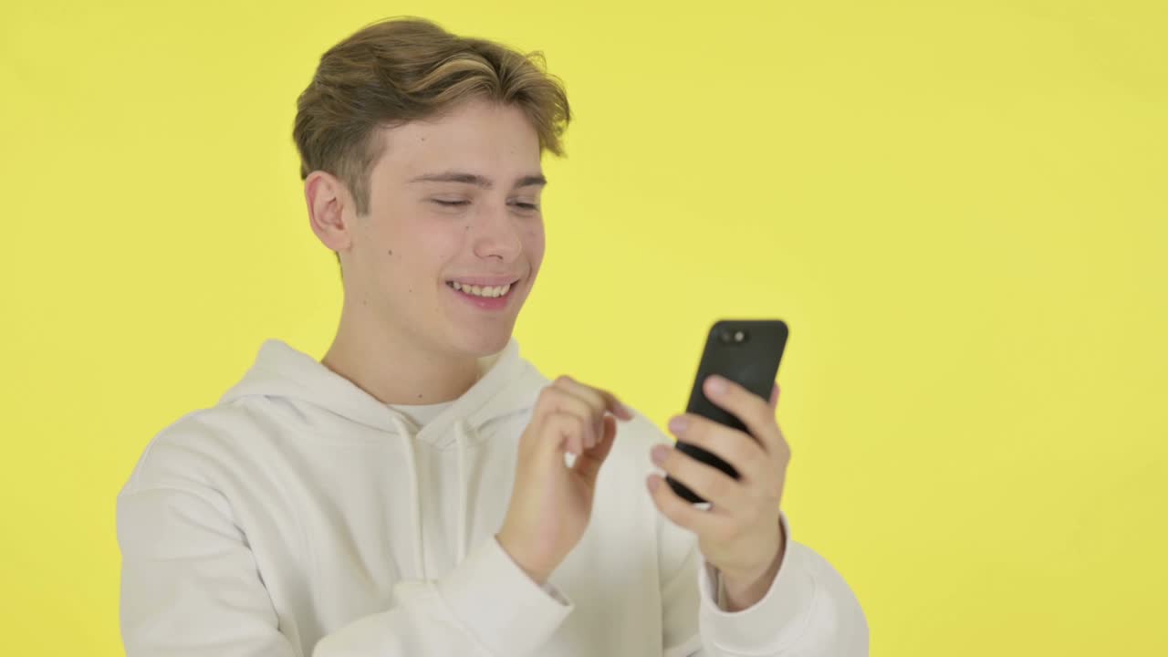 노란색 배경에 스마트폰으로 축하하는 젊은 남자