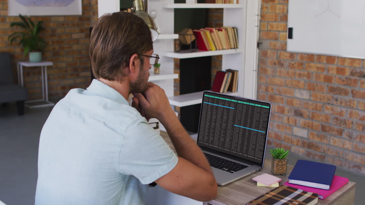 hombre caucásico sentado en el escritorio viendo el procesamiento de datos de codificación en la pantalla del portátil