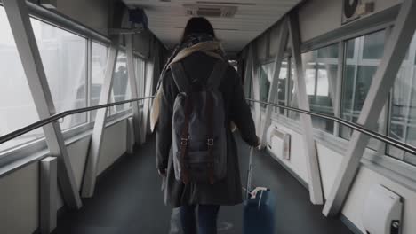 camera follows young happy tourist woman walking along modern airport departure hall corridor with suitcase slow motion.