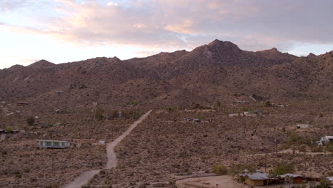 flyover a dirt road in the dessert over houses and towards jagged hills in joshua tree, california at sunrise