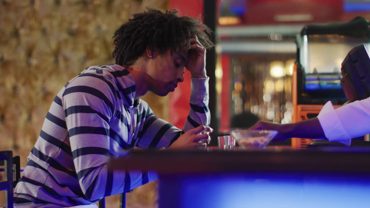 video delle mani del barista afroamericano che serve e dell'uomo ubriaco seduto a bere shot al bar