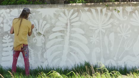 Video-of-rear-view-of-caucasian-male-artist-with-dreadlocks-painting-mural-on-wall