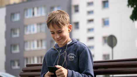 adolescente sonriente sentado en el banco, escuchando y disfrutando, asintiendo con la cabeza a la buena música con el teléfono en las manos, cerrar