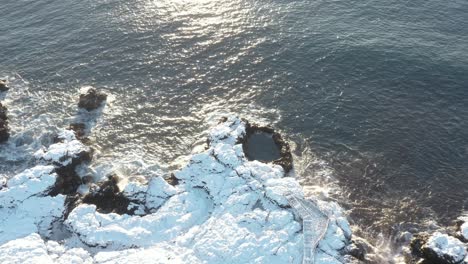 scenic rock pool on wild coast of iceland covered in white snow with sunlight