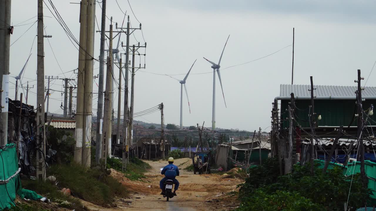 Person on a motorbike on a dirt road with wind turbines in the background