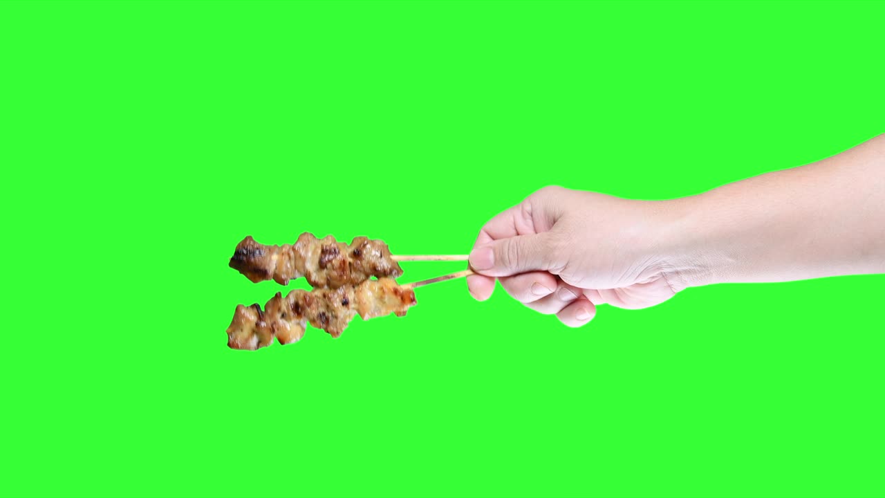 초록색 스크린 배경에 바베큐 사타이 을 들고 있는 손.