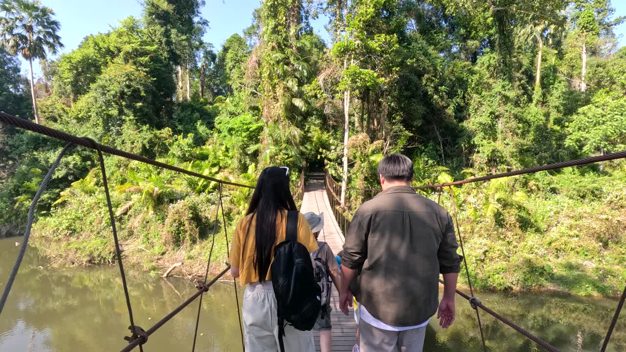 Um homem e uma mulher se afastam da câmera enquanto atravessam uma ponte suspensa na Tailândia