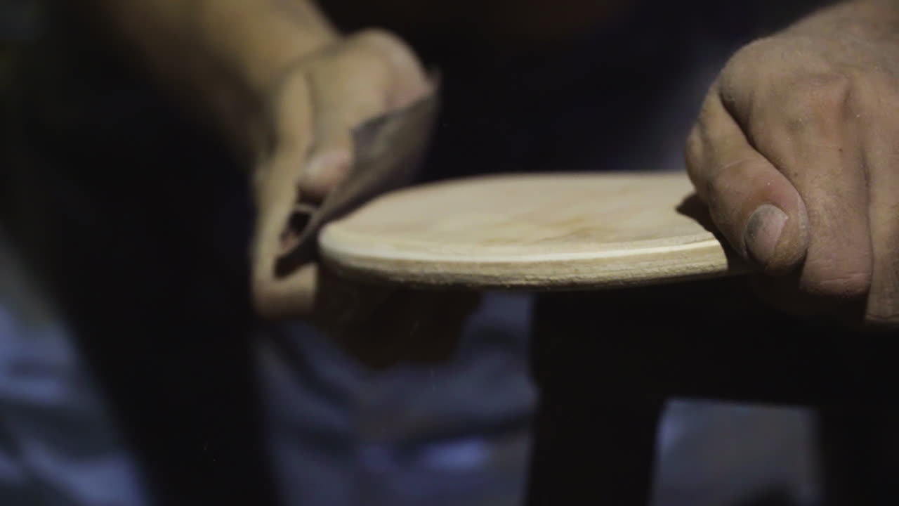 cerca, las manos del hombre manualmente lijando el lado de la tabla de patinaje diy tabla de madera con papel de lija