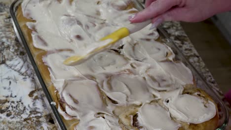 spreading cream cheese icing on freshly baked cinnamon rolls